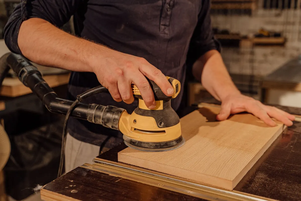 Random-orbit sander smoothing the surface of a hardwood furniture panel in a workshop
